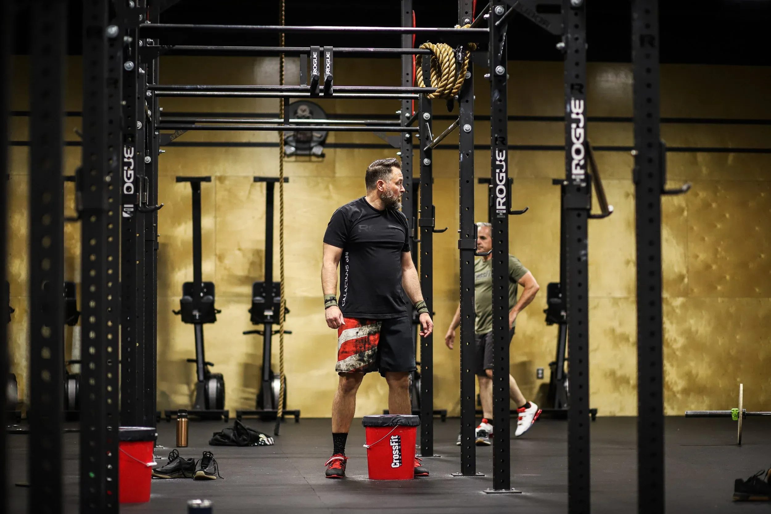 A VHSP coach watches over the floor during a class, with rigs and rowers behind him